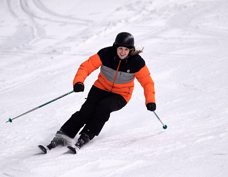 Male skier in orange jacket skiing down a snow slope from right to left